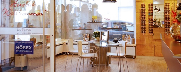 Modernes Hörakustik-Fachgeschäft mit Beratungstisch, Brillenwand und freundlicher Atmosphäre.